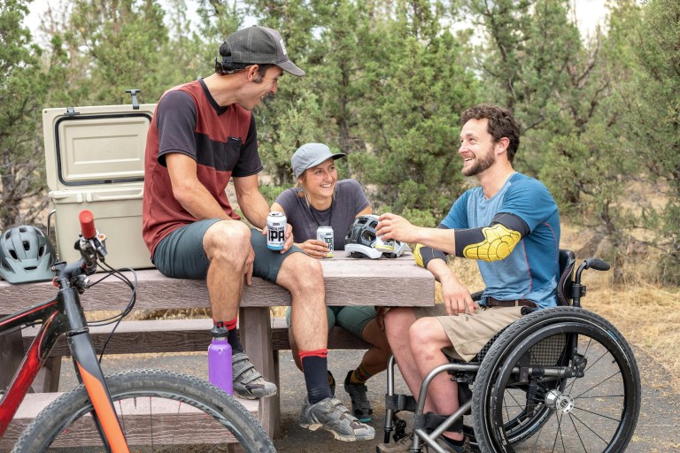 Een rolstoelgebruiker met twee anderen bij een picknicktafel