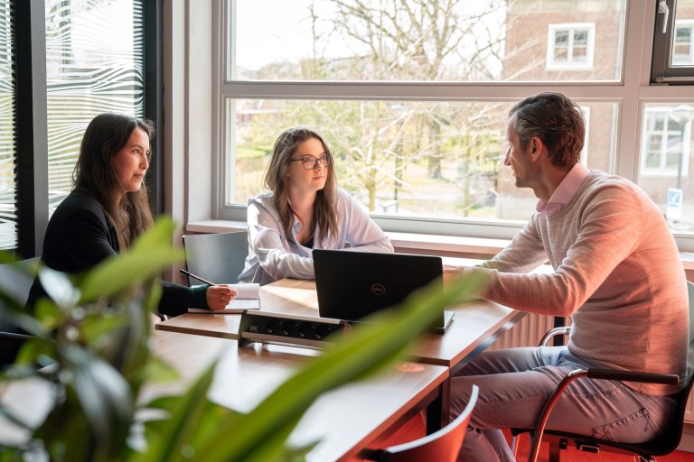 Een docent zit aan tafel met twee studenten