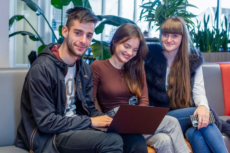 Drie studenten zitten met een laptop op een bank