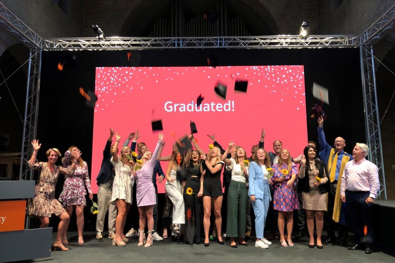 Afgestudeerde studenten gooien hun afstudeerhoed in de lucht