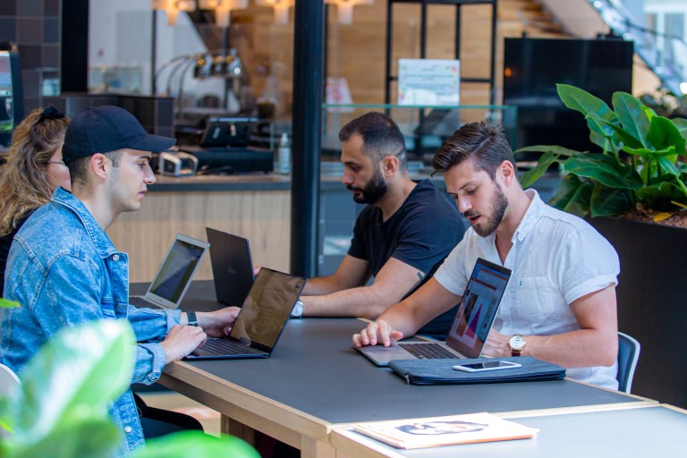 Vier studenten werken op hun laptop aan een tafel 