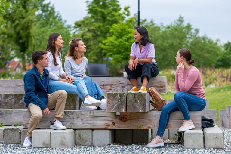 Vijf studenten zitten op een bank op de BUas campus