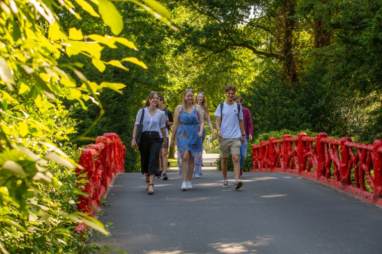 Een groep studenten loopt over een brug in een park 