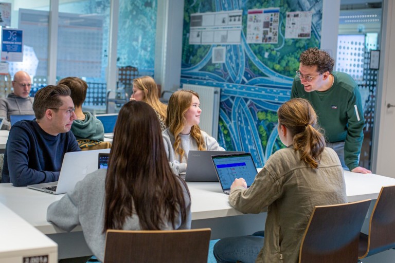 Een docent staat bij studenten aan een tafel