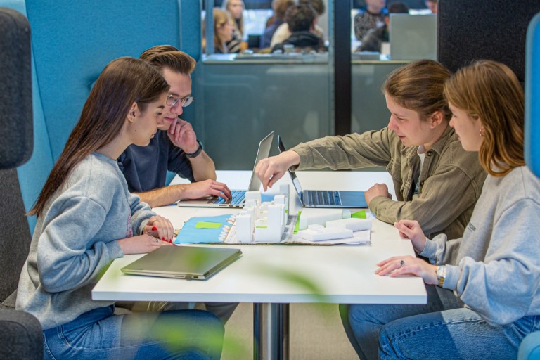 Vier studenten werken aan een schaalmodel van gebouwen