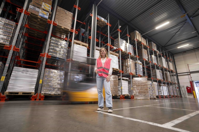 Een student staat in een magazijn met hoge stellages 