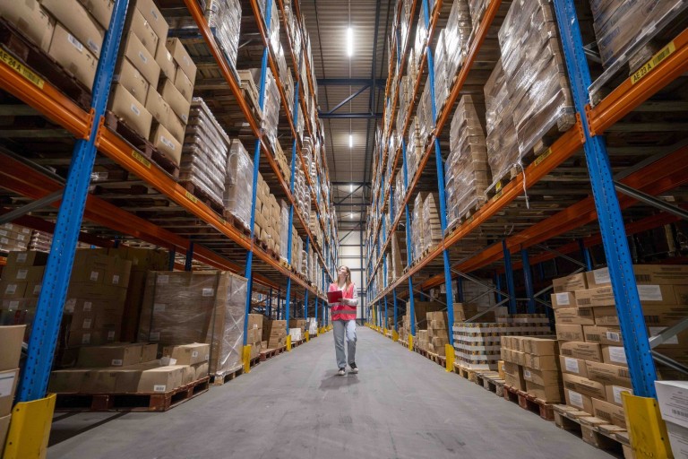 Een student staat in een magazijn met hoge stellages