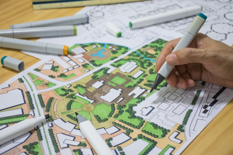 Een hand werkt met een stift aan de plattegrond van een wijk