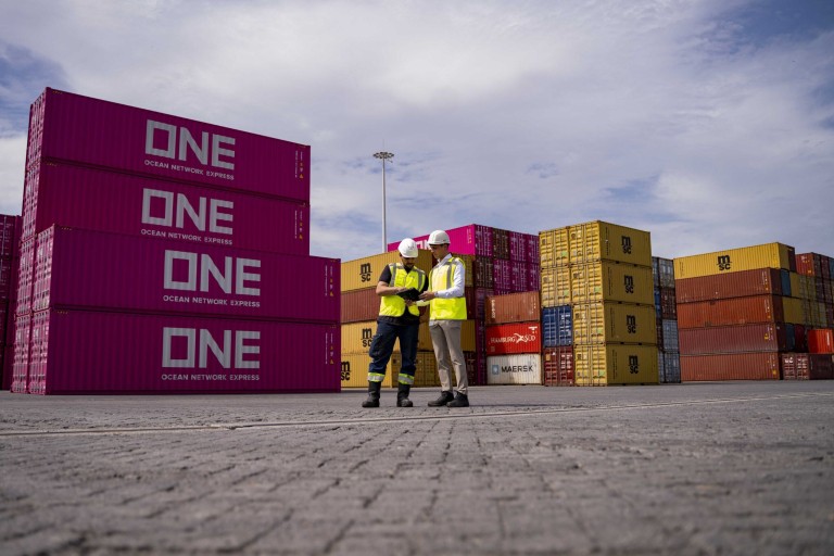 Twee mannen staan naast containers in een haven