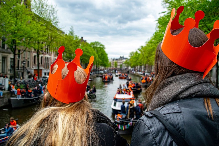 Twee meisjes met een oranje kroon kijken naar varende boten