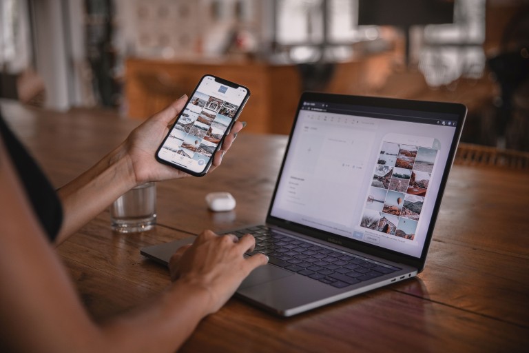 Iemand houdt zijn telefoon naast zijn laptop