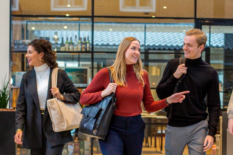 Vijf studenten lopen met hun tassen door de school