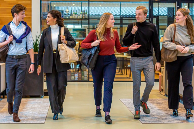 Vijf studenten lopen met hun tassen door de school