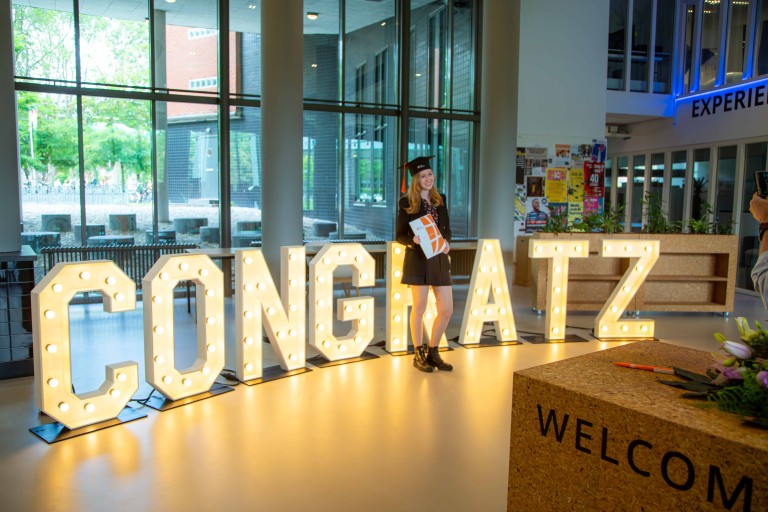 Een afgestudeerde student poseert voor de letters 'Congratz'