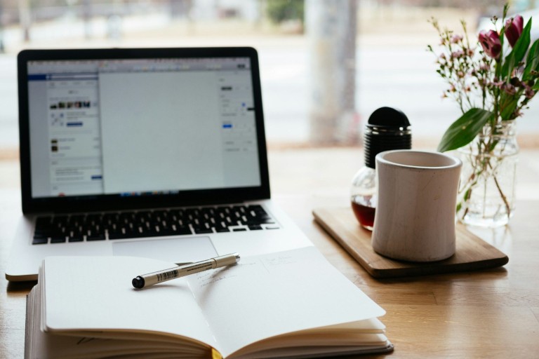 Een laptop en een schrift liggen op een tafel