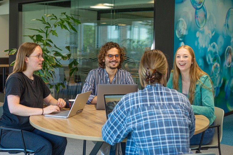 Vier studenten werken aan een ronde tafel