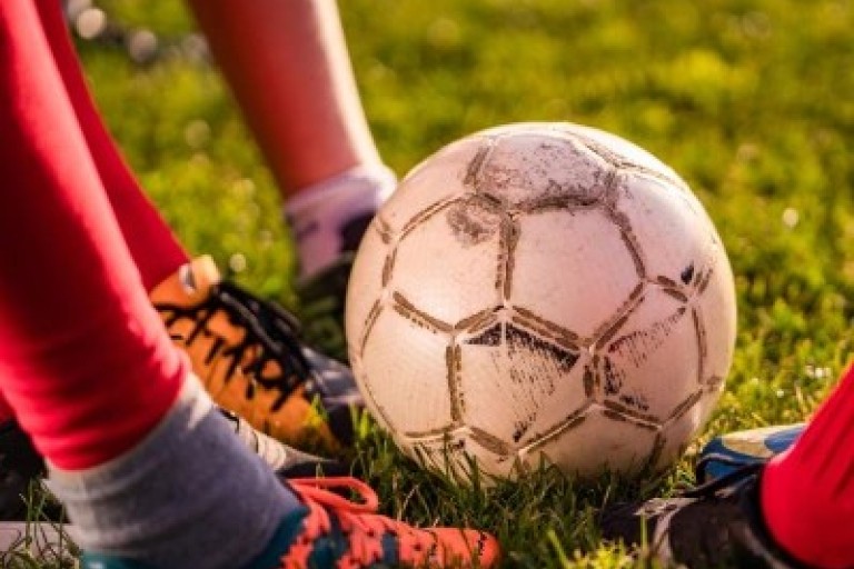 Vier voeten met voetbalschoenen staan naast een voetbal