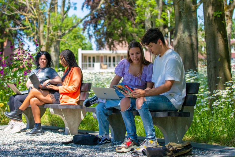 Vier studenten zitten op een bankje buiten op de BUas campus