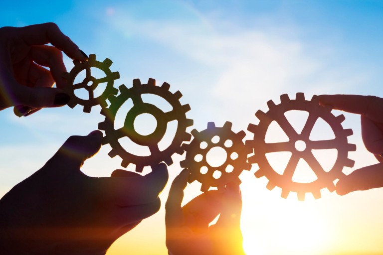 Vier handen houden tandwieltjes vast die in elkaar passen