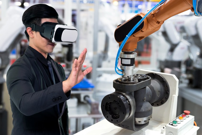 Een persoon met een VR bril op staat voor een robotarm