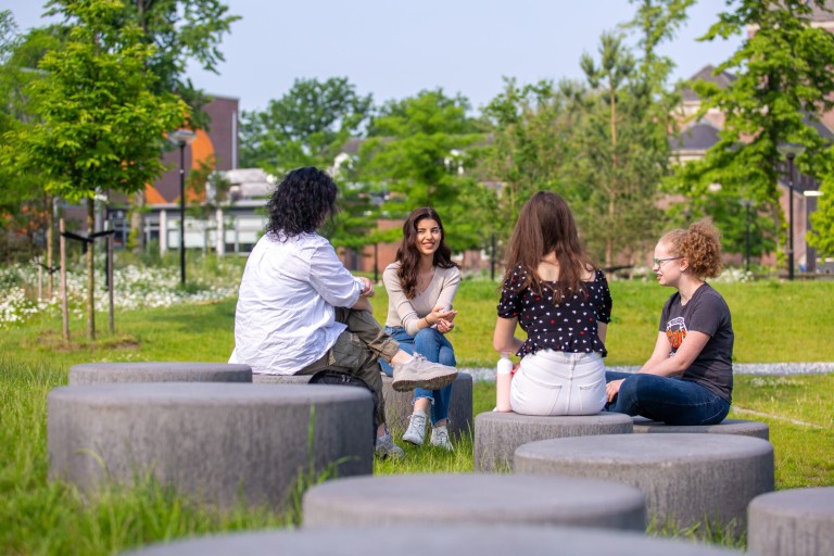 Een groepje studenten zit buiten bij de campus