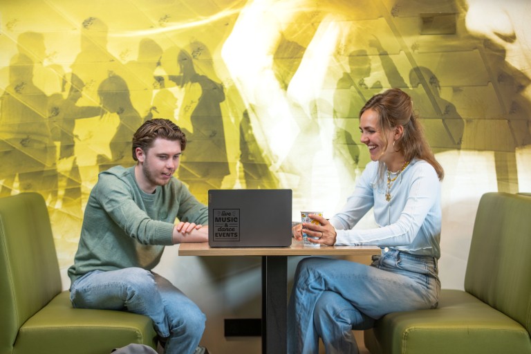 Twee studenten lachend aan het werk achter een laptop