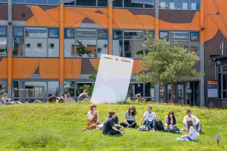 campus gebouw met oranje graffiti met daarvoor studenten in het gras