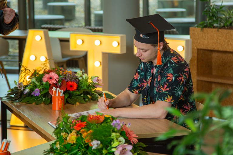 Een student zet een handtekening onder zijn diploma