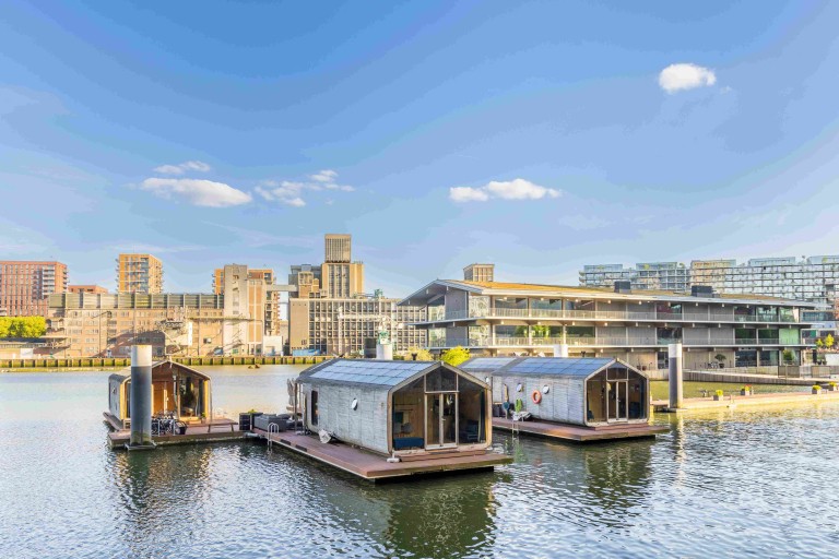 Drijvende woningen met zonnepanelen op het water, met een stadsgezicht op de achtergrond.