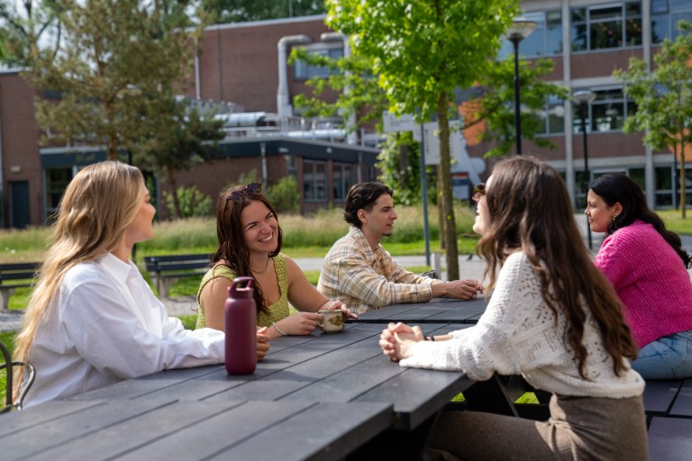 students at a picnic table sitting outside laughing