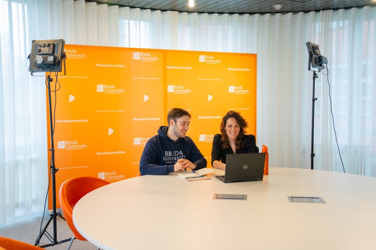 two people with laptop in front of orange screen