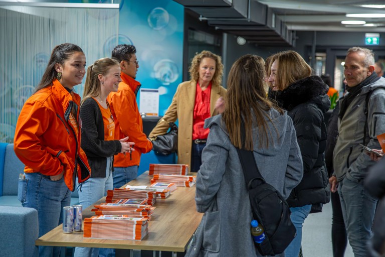 students with orange jackets behind a table with flyers