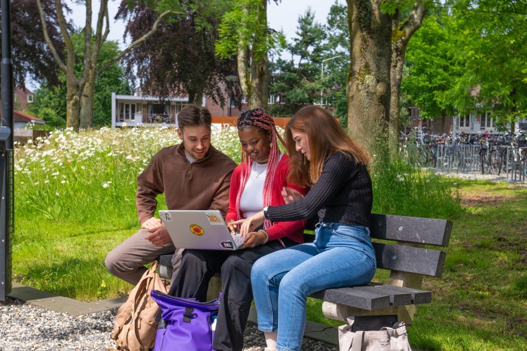 three students with a laptop on a bench