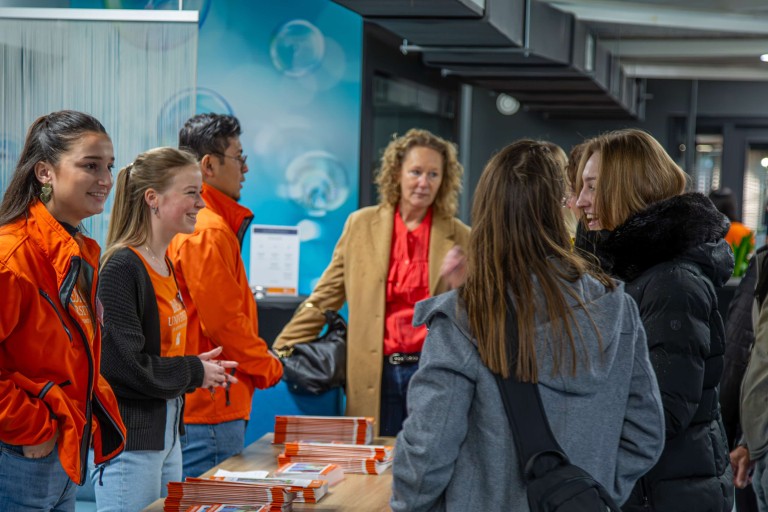 students with orange jackets behind a table with flyers