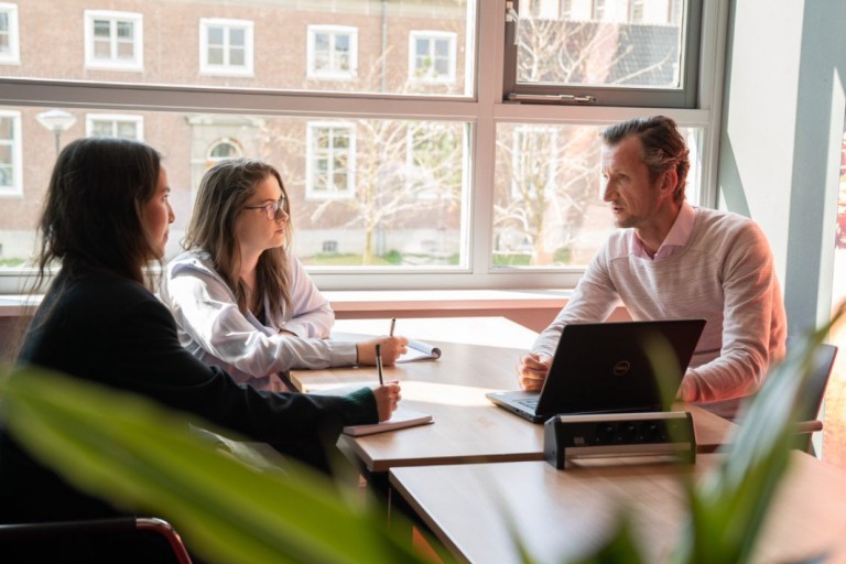 Twee studenten praten met een docent over hun werk