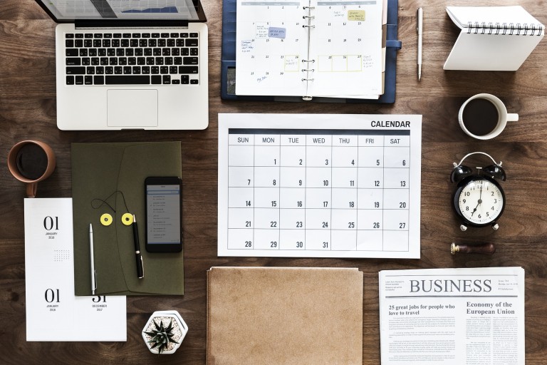 Een tafel met kantoorspullen, een kalender, krant en klok