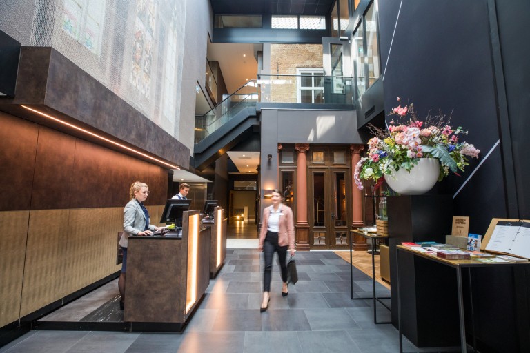 Een vrouw loopt langs een balie met twee medewerkers 