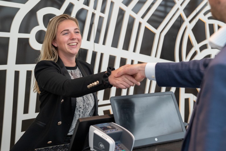 Een vrouw achter een balie geeft een man een hand