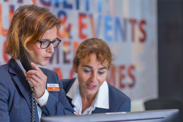 Twee vrouwen staan met een telefoon achter een balie