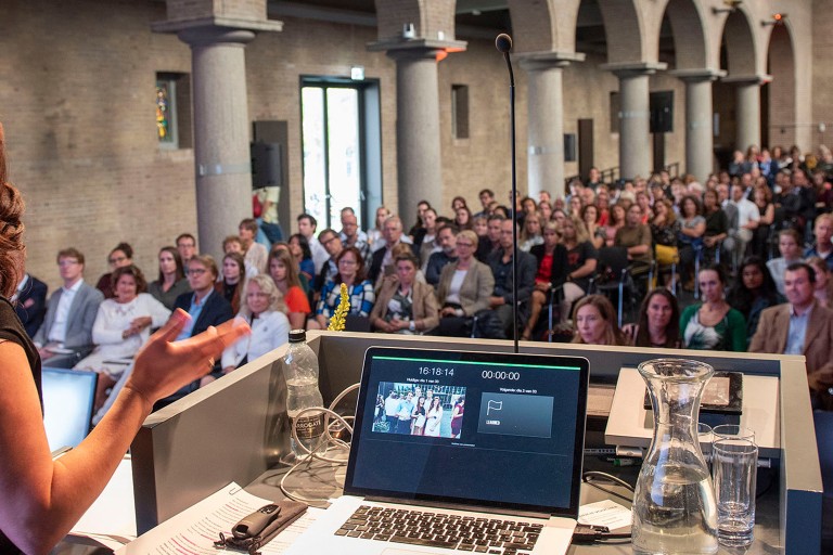 Een vrouw geeft een presentatie voor een grote zaal