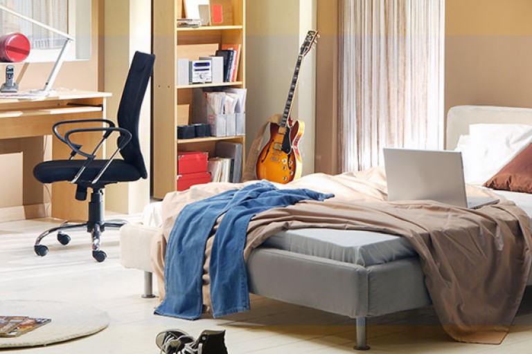 Een rommelige slaapkamer met een bed, bureau en stoel