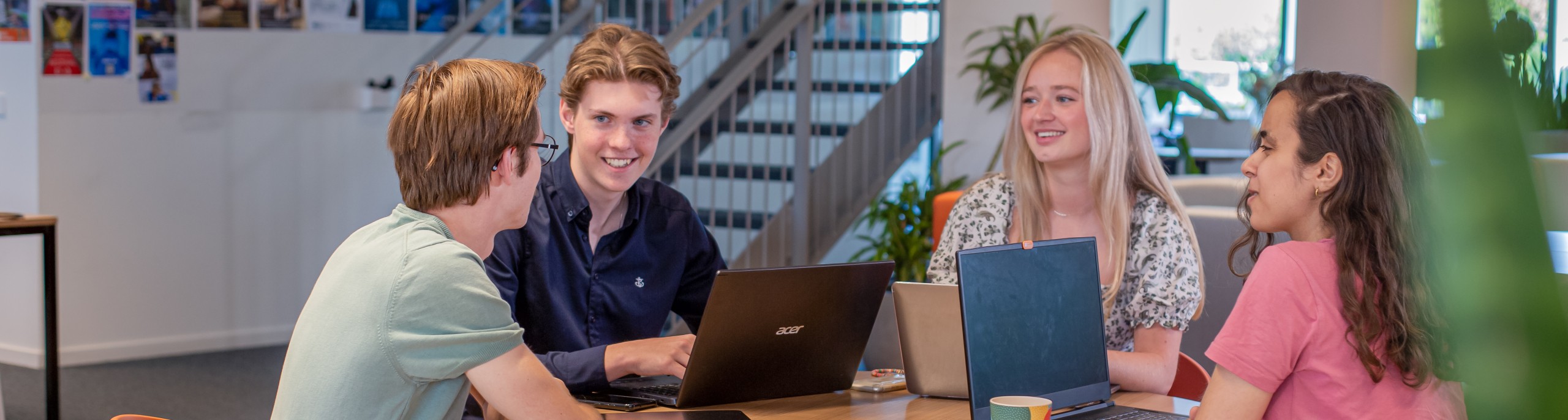 Vier studenten werken samen op laptops aan een tafel