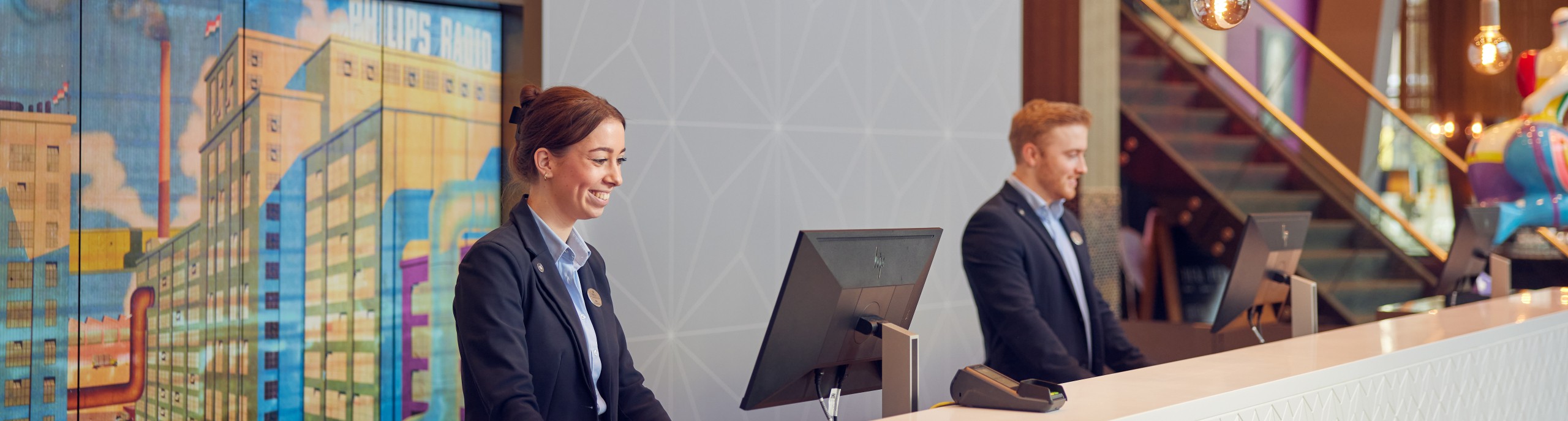 Twee mensen staan achter een receptiebalie 