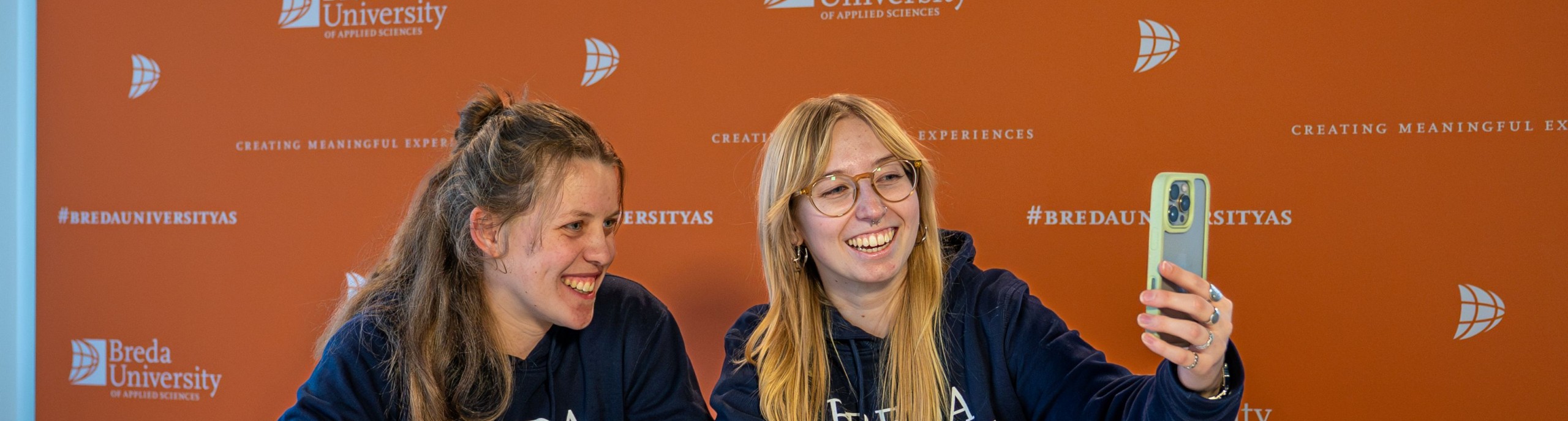 Twee student ambassadors lachen voor een telefoon