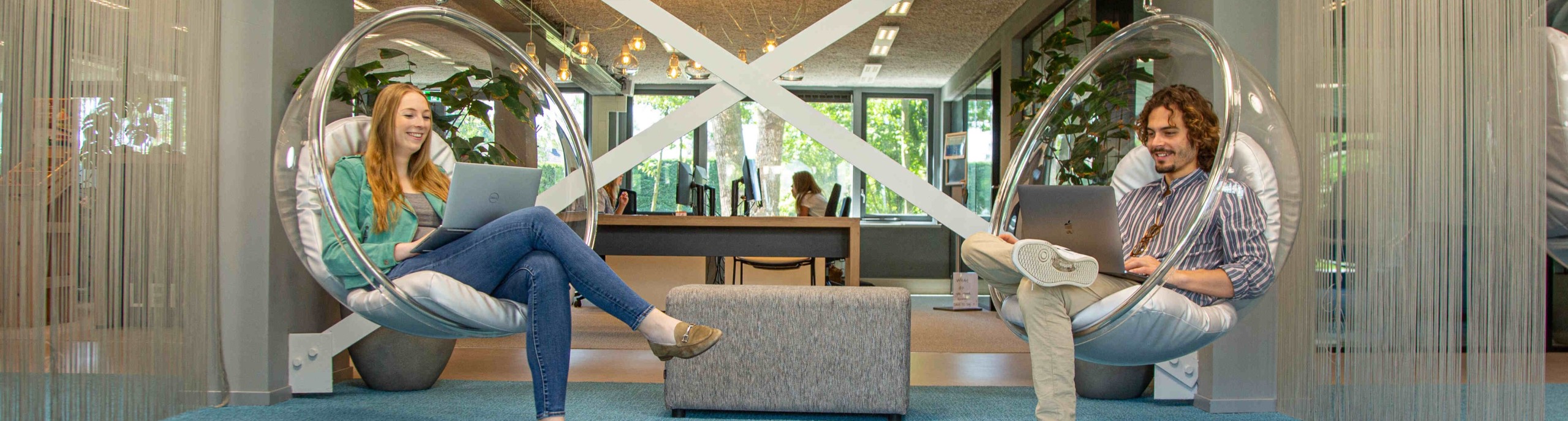 Twee studenten zitten in glazen hangstoelen 