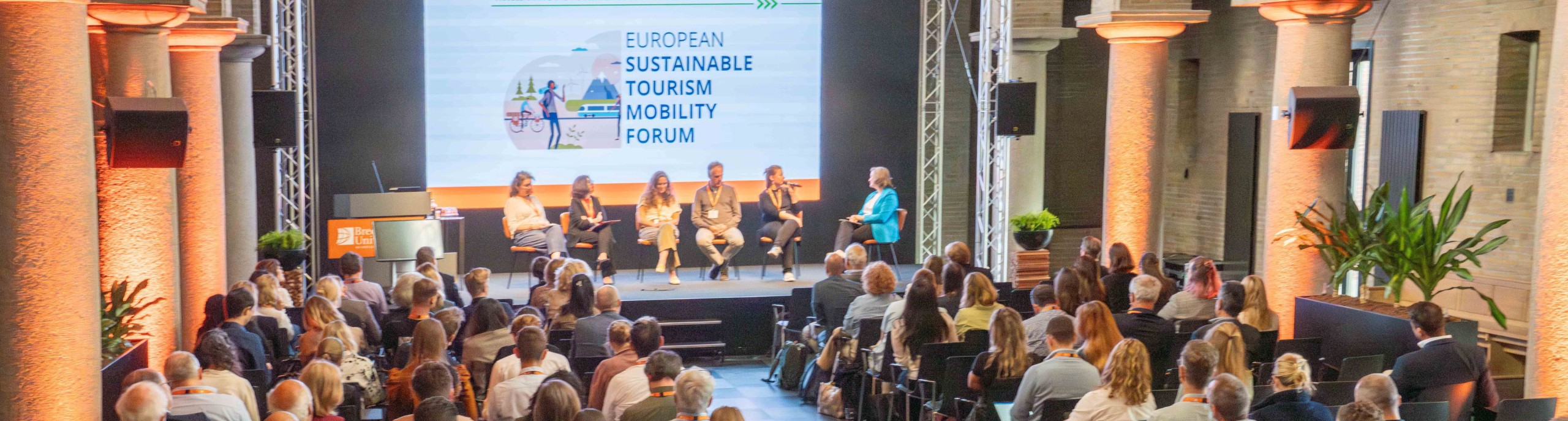 Een zaal vol deelnemers luistert naar sprekers op het podium