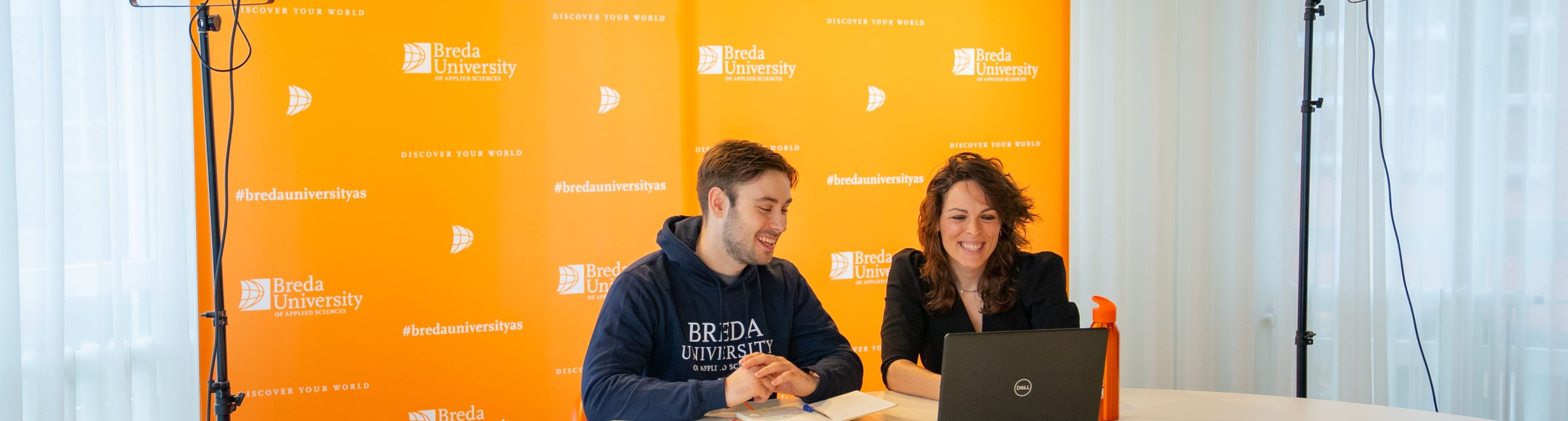 two people with laptop in front of orange screen