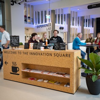 Studenten en docenten zitten samen aan statafels 