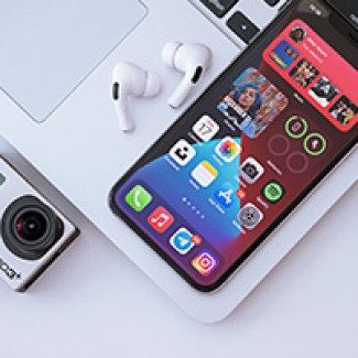 Een telefoon, laptop, camera en AirPods liggen op een tafel 