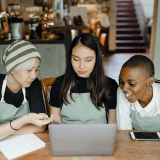 Drie vrouwen in schorten werken samen op een laptop